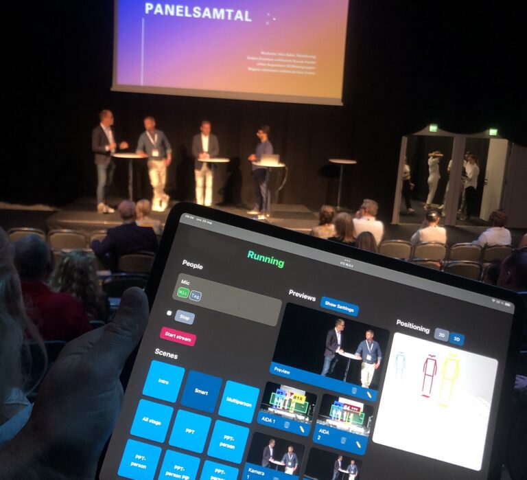 En panel på scen, med produktionskontrollerna på en surfplatta i förgrunden